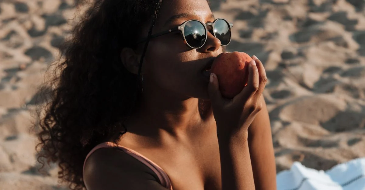 Une jeune femme se détend sur la plage, savourant une pêche sous le soleil éclatant.