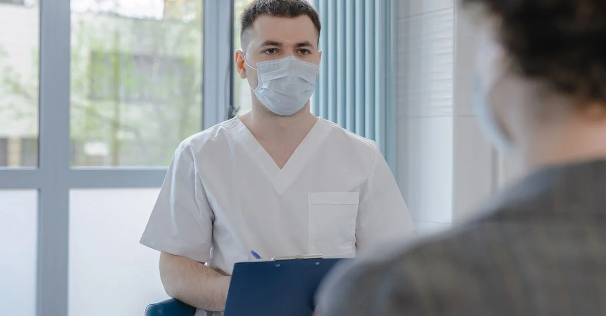 Professionnel de la santé en tenue médicale consultant un patient tout en prenant des notes.