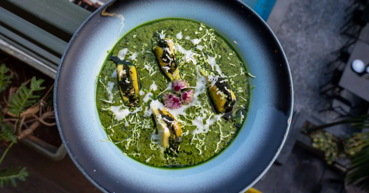 Vue aérienne de cannellonis aux épinards et au fromage, garnis de fleurs, présentés dans un bol gris.