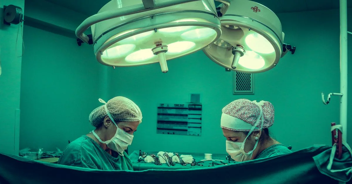 Chirurgiens dans une salle d'opération effectuant une procédure médicale sous des lumières chirurgicales vives.