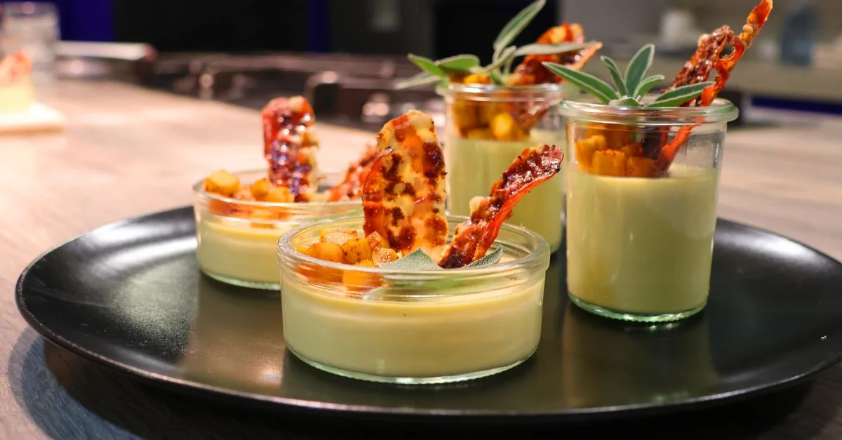 Dessert gourmand élégant servi dans des bocaux en verre avec garniture caramélisée et herbes.
