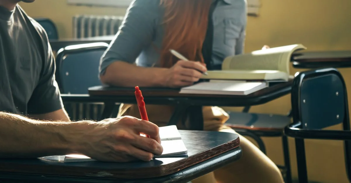 Deux étudiants prennent des notes et lisent pendant le cours, ce qui témoigne de leur concentration et de leur intérêt pour l'éducation.