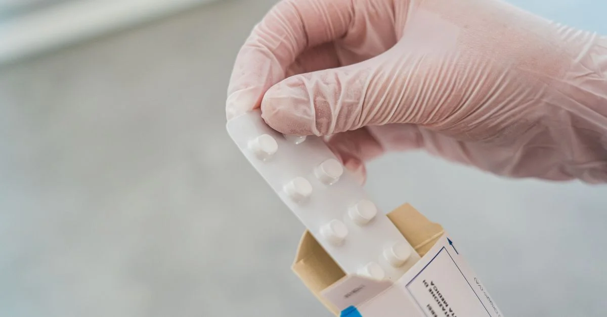 Gros plan sur une main gantée tenant une plaquette de médicaments, symbolisant les soins médicaux.