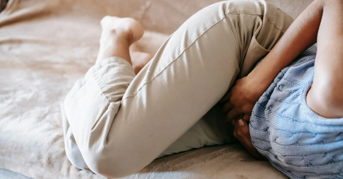 Une personne en douleur tenant son ventre en étant allongée sur un canapé à l'intérieur, suggérant un inconfort ou une maladie.