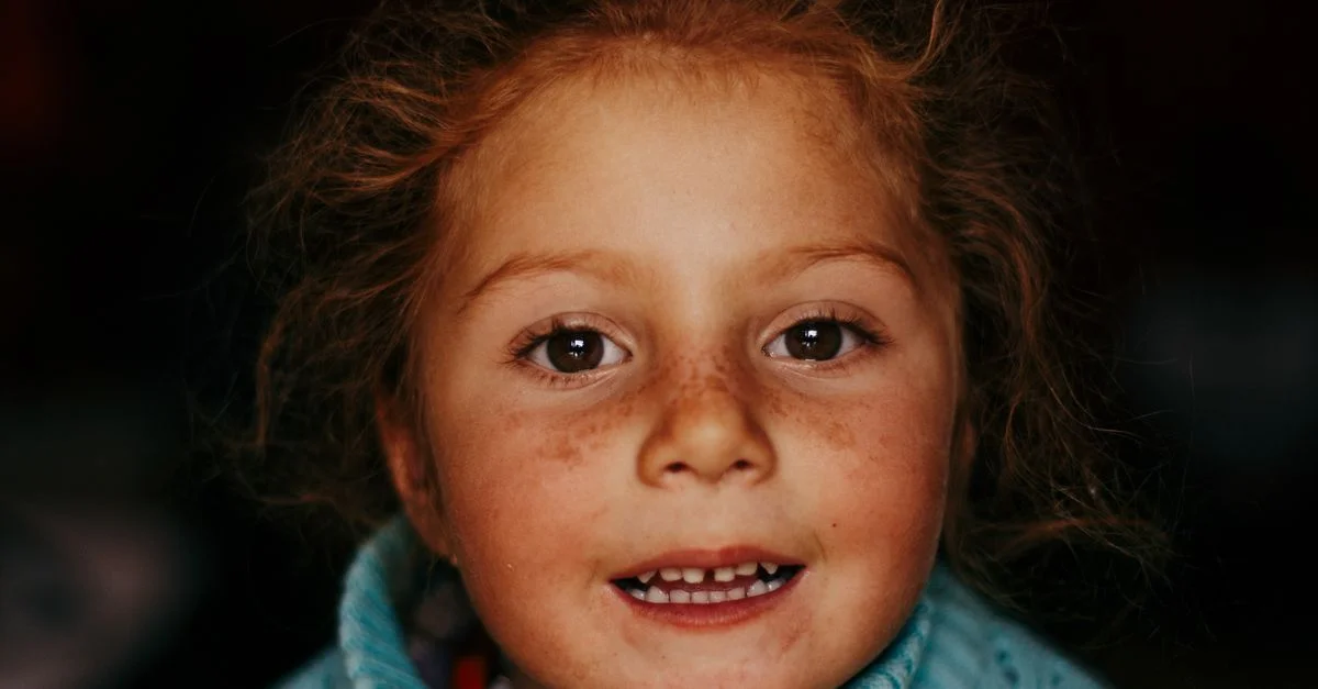 Portrait adorable d'une fille souriante avec des taches de rousseur et des cheveux bouclés.