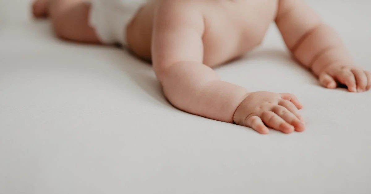 Gros plan sur un bébé dans une couche rampant sur une surface douce et blanche à l'intérieur.