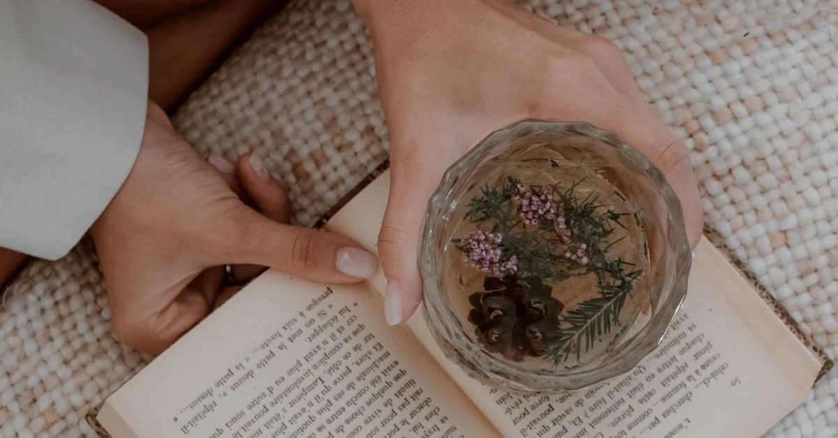 Une vue apaisante en plongée de mains tenant une tisane au-dessus d'un livre ouvert, évoquant la détente.