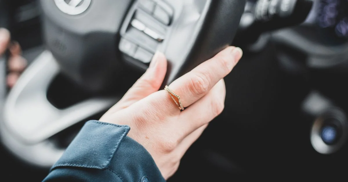 Un gros plan d'une main portant une bague en or sur le volant d'une voiture à l'intérieur d'un véhicule.