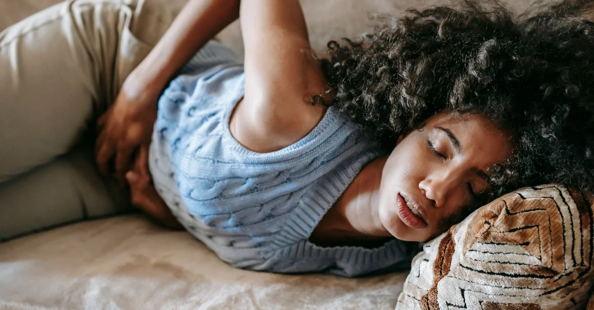 Une femme allongée sur un canapé ressentant des douleurs abdominales, reflétant l'inconfort et le repos.