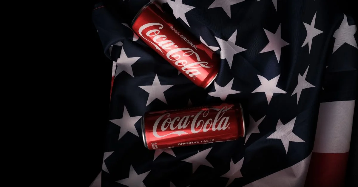 Des canettes rouges de Coca Cola affichées sur un drapeau américain symbolisant le patriotisme et la reconnaissance de la marque