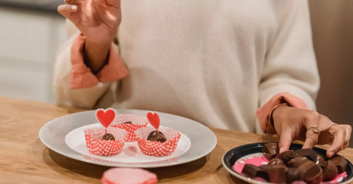 Une femme arrange des chocolats sur le thème des cœurs sur une table en bois, parfaits pour la célébration de la Saint-Valentin.