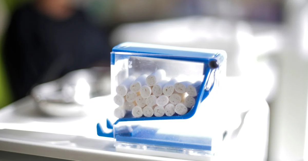 Gros plan sur des rouleaux de coton dentaire dans un distributeur bleu transparent sur une table de clinique, avec un arrière-plan flou.