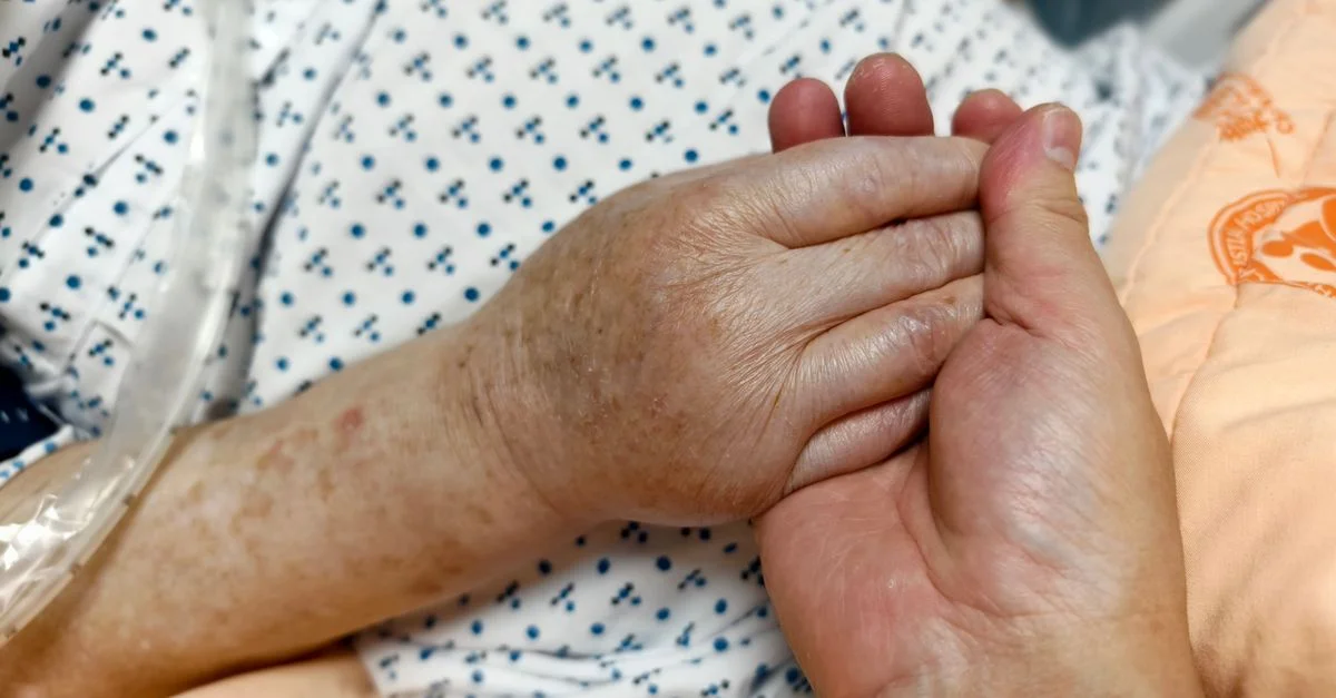 Gros plan de mains qui se tiennent dans un cadre hospitalier, symbolisant compassion et soin.