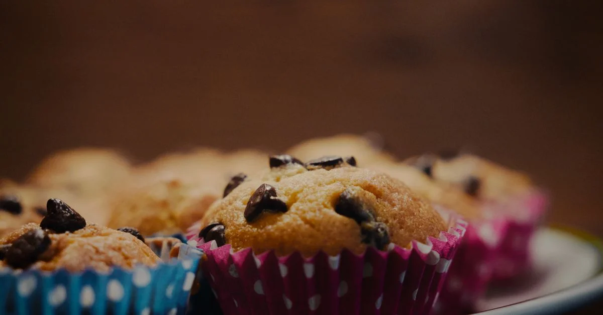 Gros plan sur des muffins aux pépites de chocolat fraîchement cuits dans des emballages à pois sur une assiette.
