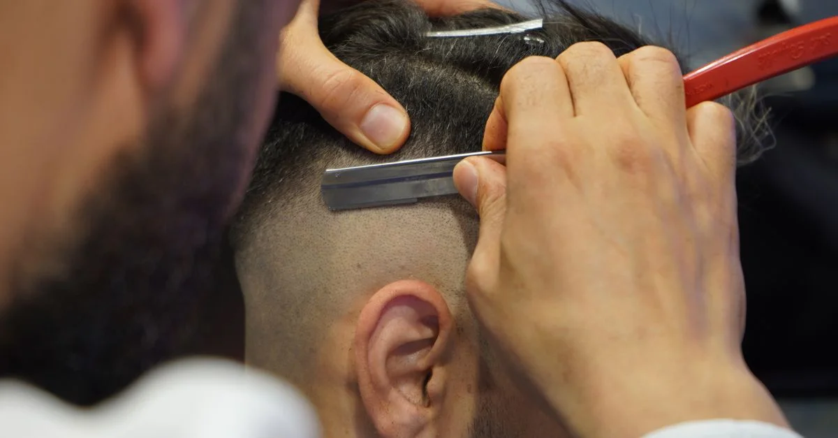 Un gros plan d'un barbier en train de raser les cheveux d'un homme avec un rasoir droit.