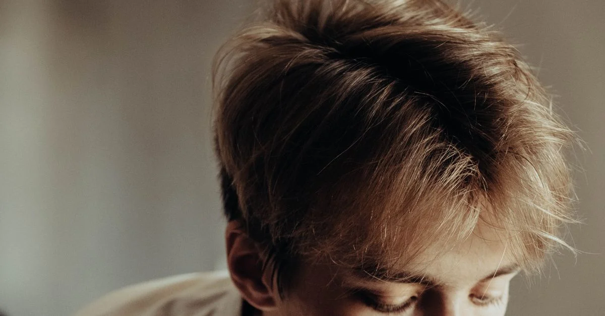 Une image en gros plan détaillée mettant en avant la coupe de cheveux stylée d'un jeune homme avec des cheveux châtains clairs ébouriffés.