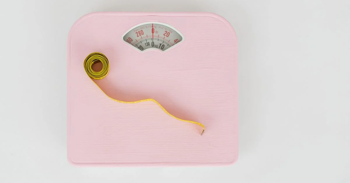 Une balance rose associée à un ruban à mesurer jaune sur un fond blanc.