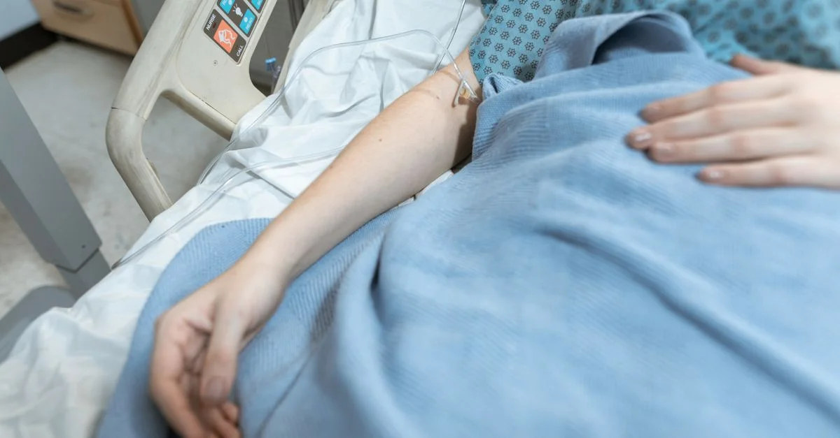 Gros plan sur un patient dans un lit d'hôpital recevant un traitement intraveineux, évoquant les soins de santé et la récupération.