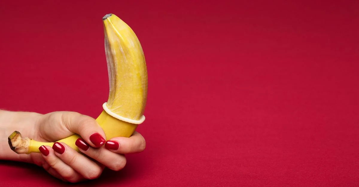 Représentation créative du sexe sûr utilisant une banane avec un préservatif sur fond rouge.