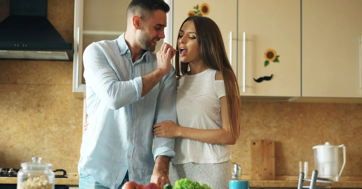 Joli couple partageant de la nourriture dans une cuisine confortable, affichant affection et joie.