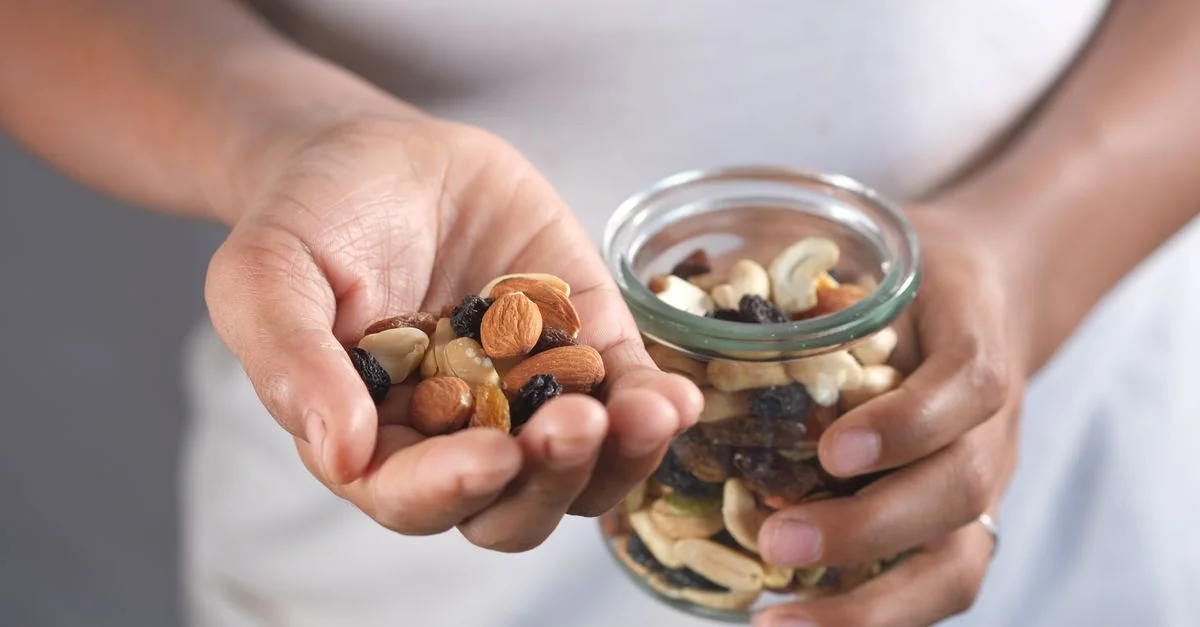 Des mains tenant un pot en verre et une poignée de noix assorties, parfaites pour une collation saine.