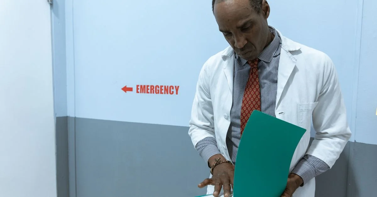Un médecin en blouse blanche examine des documents près du panneau des urgences.