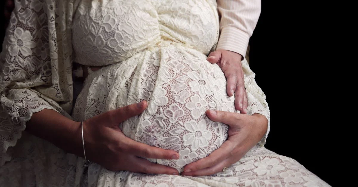 Gros plan d'une femme enceinte tenant son ventre dans une délicate robe en dentelle, symbolisant la maternité.