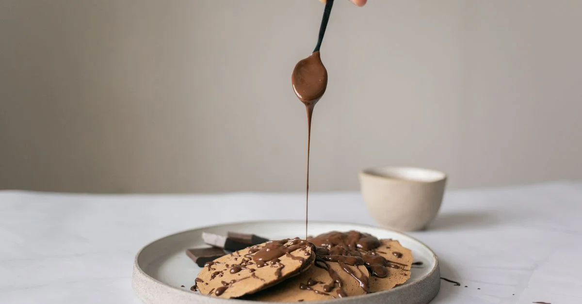 Des crêpes maison garnies de sirop au chocolat riche sur une assiette, parfaites pour un petit-déjeuner ou un dessert savoureux.