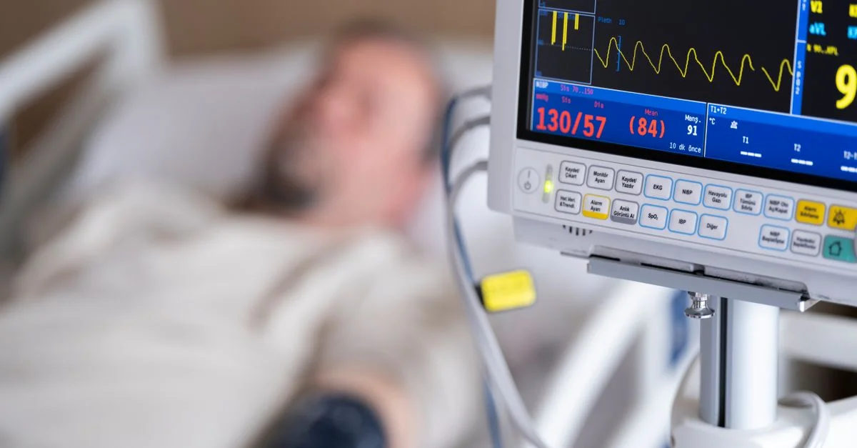 Patient dans un lit d'hôpital avec moniteur cardiaque affichant la pression artérielle et le rythme cardiaque.