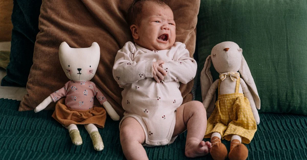 Un bébé qui pleure dans un cadre douillet avec des peluches adorables, créant une scène chaleureuse et tendre à l'intérieur.