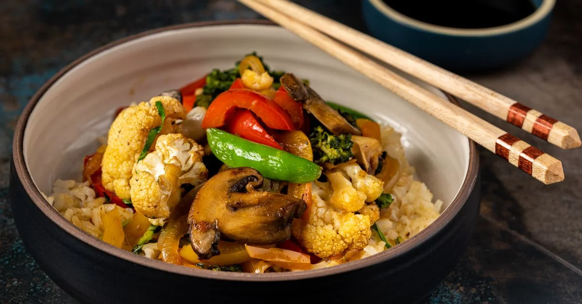Gros plan sur un bol de riz aux légumes vibrant avec des champignons et des baguettes.