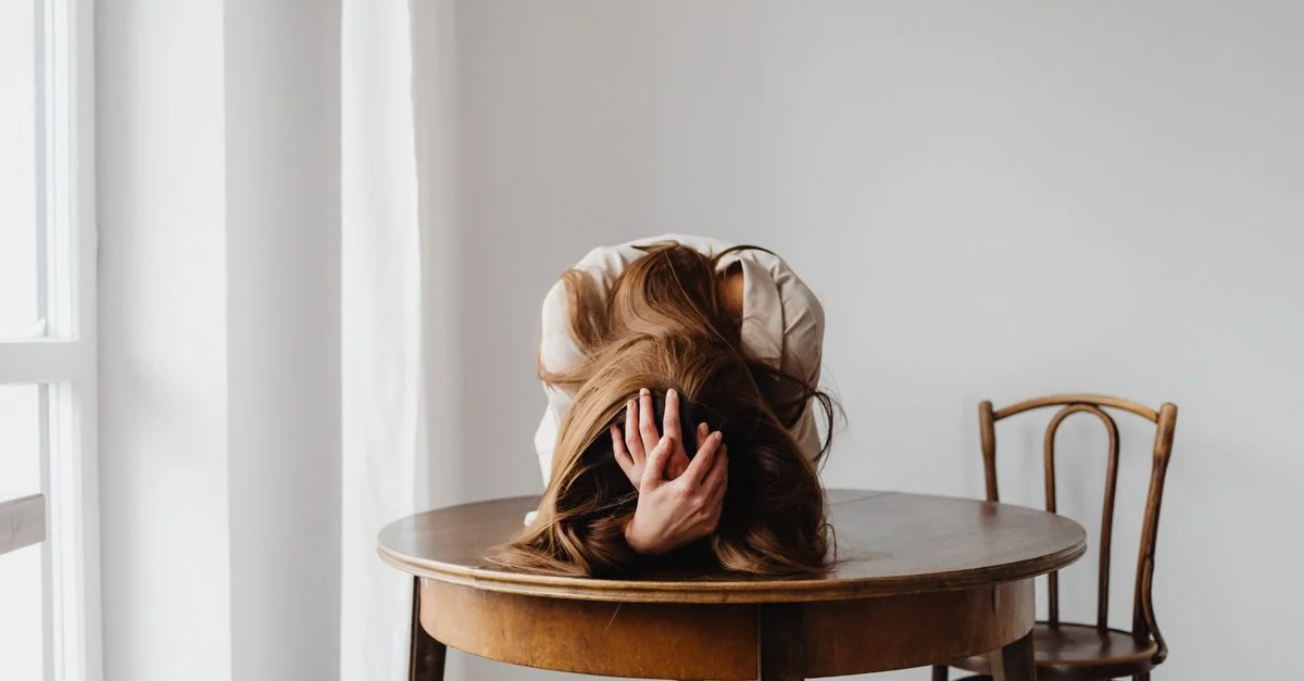 Femme penchée sur la table, mains sur la tête, symbolisant le stress à l'intérieur.