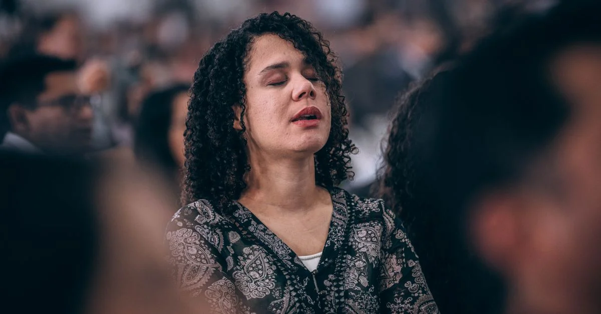 Une femme aux yeux fermés, plongée dans un moment de réflexion lors d'une réunion en intérieur.