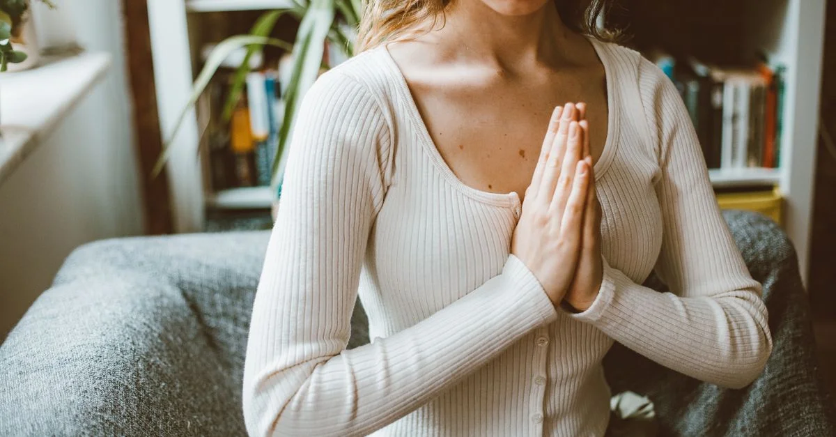 Une femme méditant à l'intérieur, se concentrant les mains en position de prière.