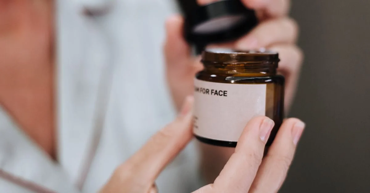 Plan détaillé des mains ouvrant un pot de crème pour le visage, mettant en valeur la routine de soin de la peau.
