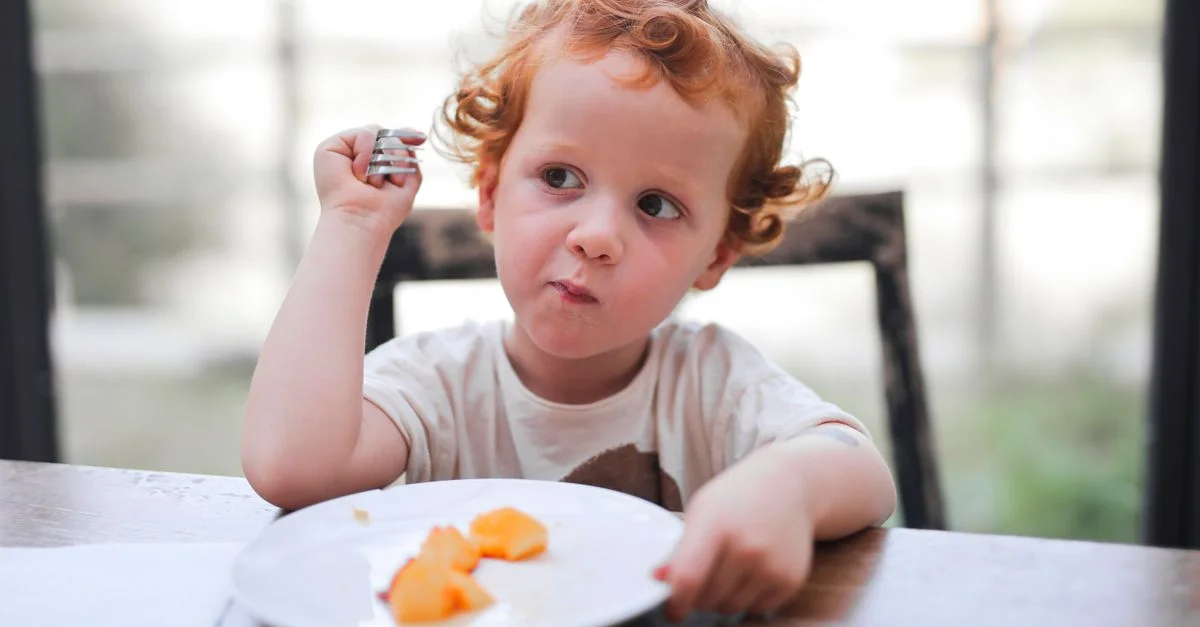 Un enfant adorable dégustant un repas à une table en bois, mettant en avant l'enfance et l'innocence.
