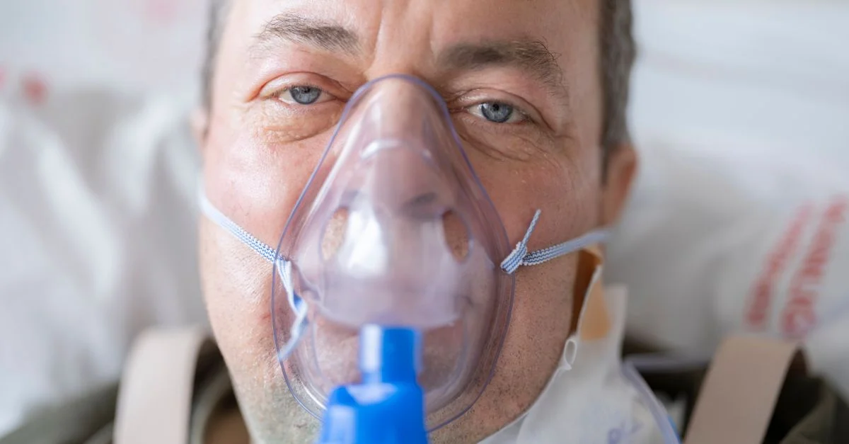 Gros plan d'un homme dans un lit d'hôpital portant un masque à oxygène, mettant en évidence les besoins en santé.