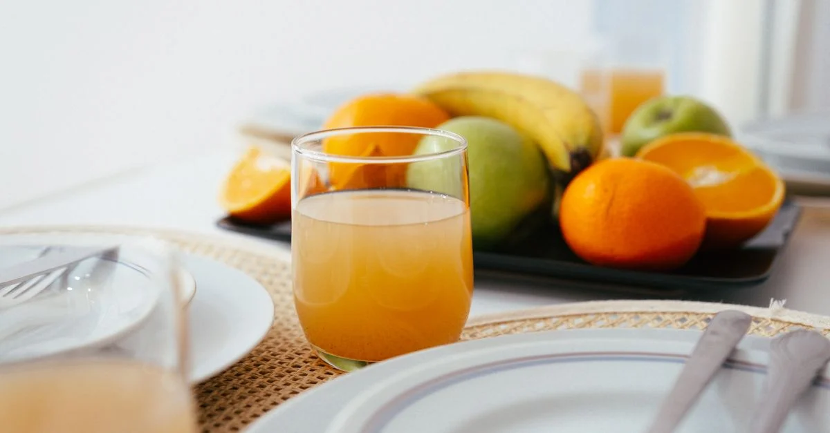 Mise en place de petit déjeuner lumineux et frais avec du jus d'orange et une variété de fruits sur une table soigneusement arrangée.