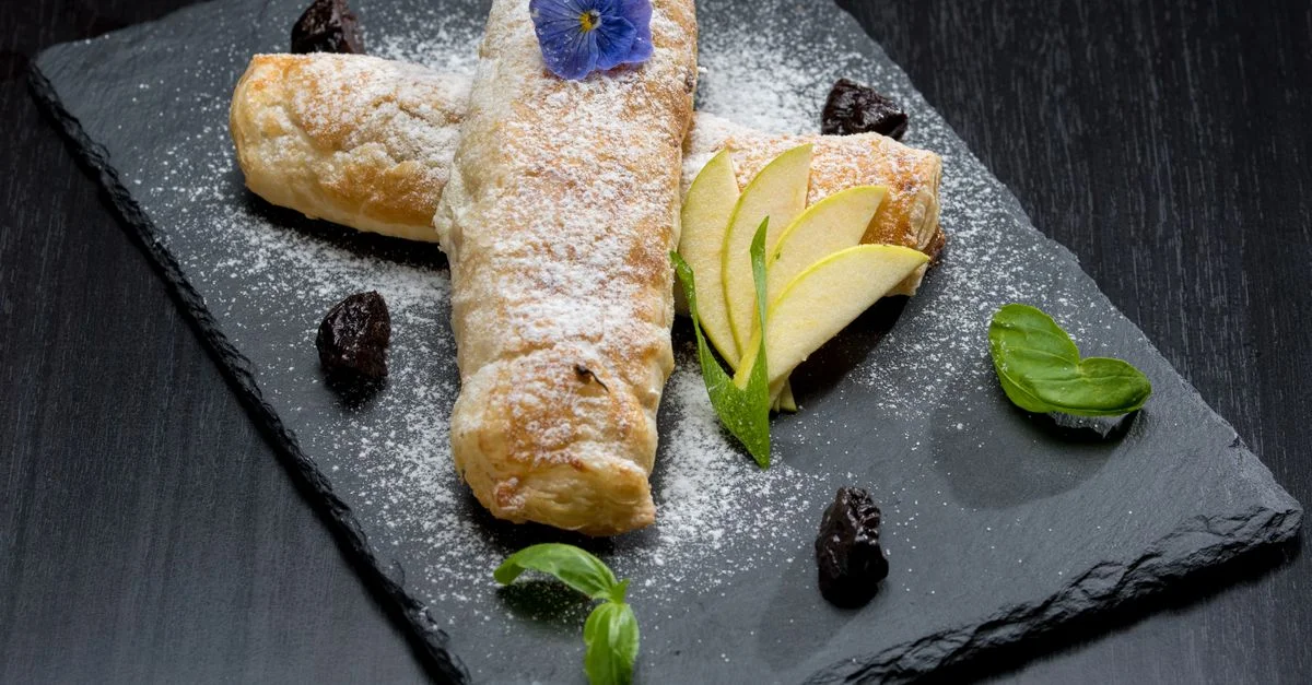Délicieuse pâtisserie surmontée de violette sur ardoise, garnie de tranches de pomme et de pruneaux.