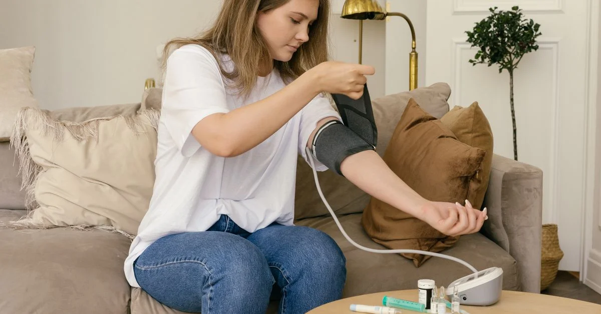 Une femme utilise un tensiomètre numérique assise sur un canapé confortable.