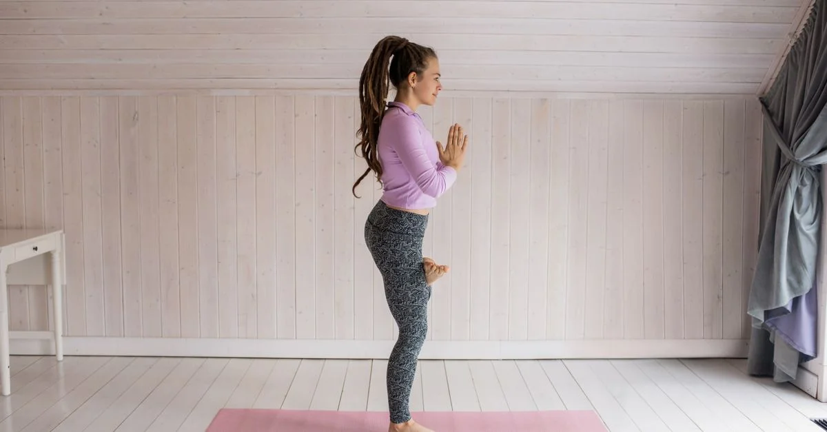 Vue de côté d'une femme faisant une posture de yoga sur un tapis à l'intérieur, incarnant l'équilibre et la forme physique.