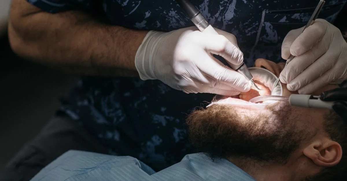 Dentiste utilisant des outils pour l'examen dentaire sur un patient masculin barbu.