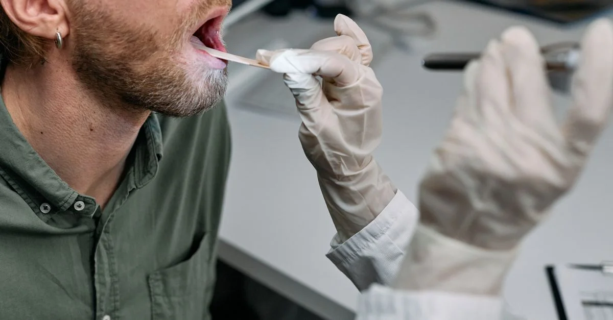 Gros plan sur un médecin examinant la gorge d'un patient avec un abaisse-langue dans un cadre clinique.