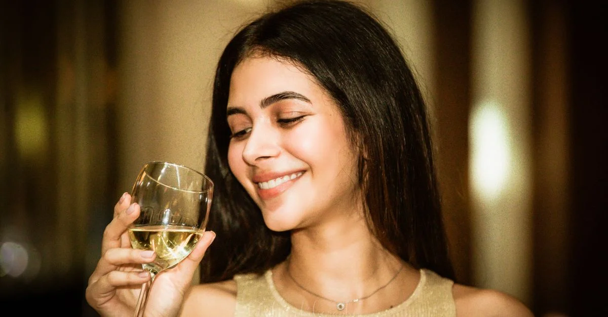 Portrait d'une femme souriante dégustant un verre de vin blanc à l'intérieur, créant une atmosphère joyeuse et détendue.