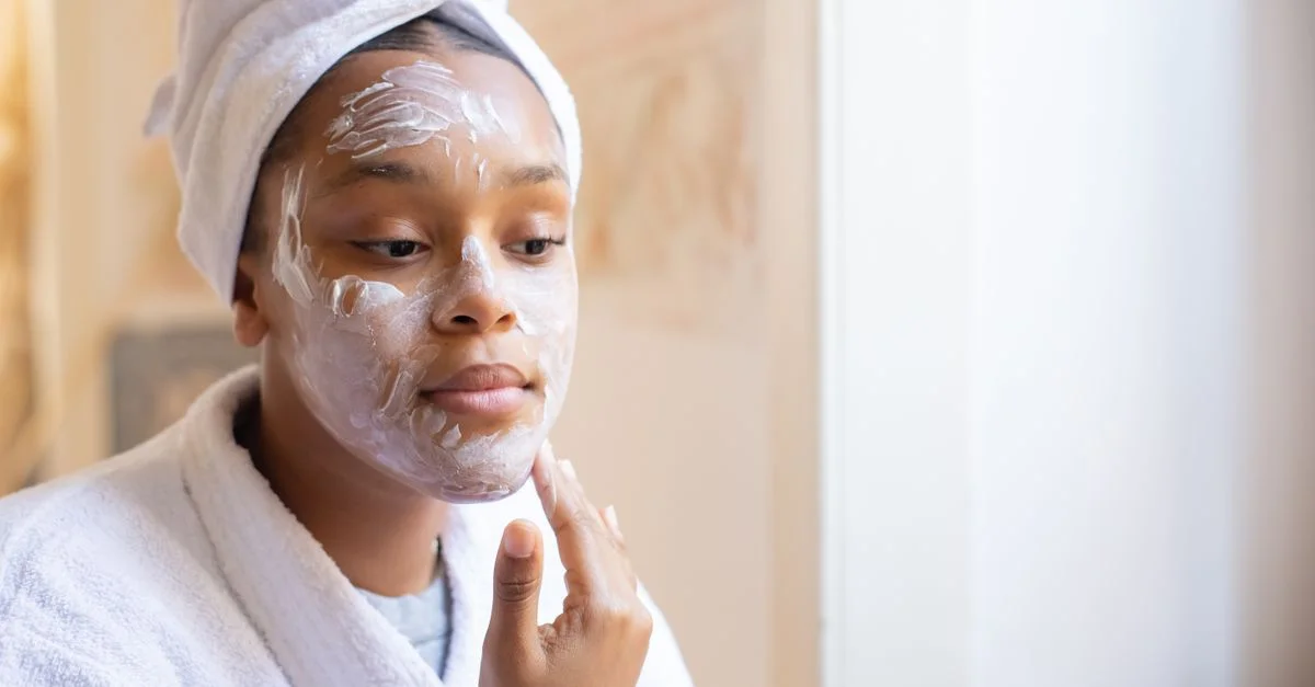 Jeune femme appliquant de la crème pour le visage pendant sa routine de soins de la peau du matin à l'intérieur.