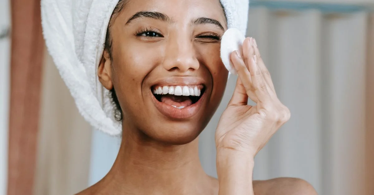 Femme souriante appliquant des soins de la peau avec un coton, promouvant des routines de soin de la peau saines.