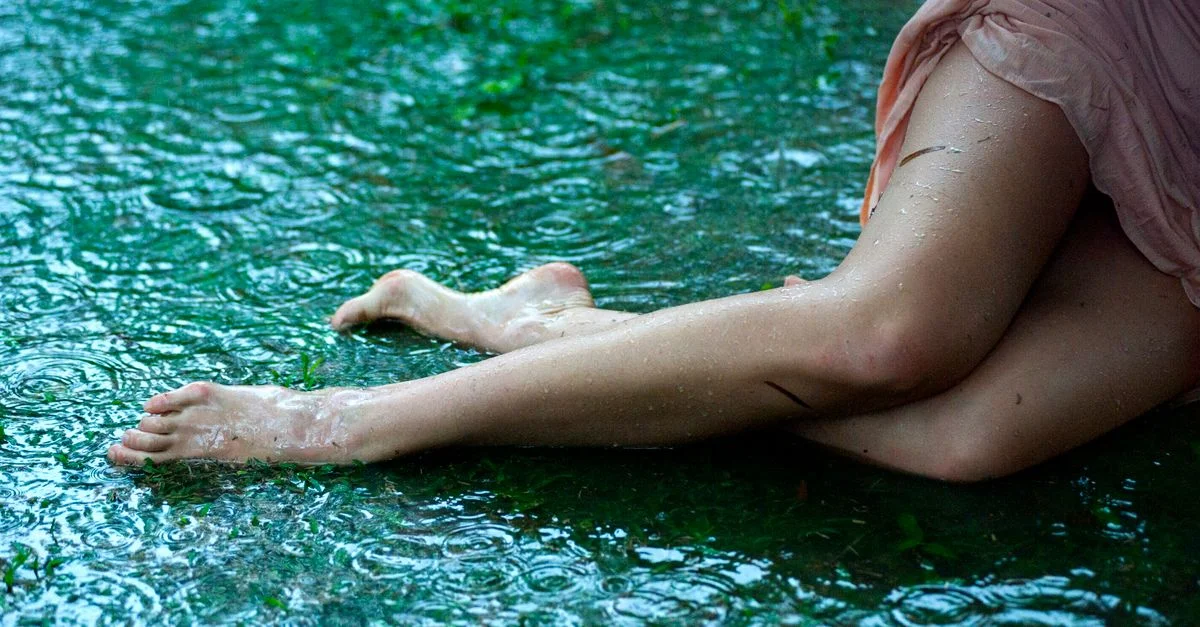 Une femme pose avec des jambes nues sur un sol humide, créant une scène artistique de pluie.