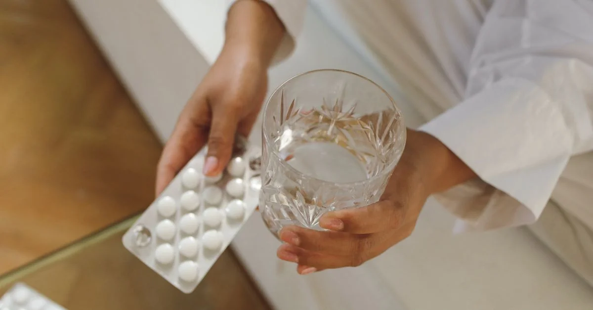 Image en gros plan de mains tenant des pilules et un verre d'eau, idéal pour des thèmes de santé et de bien-être.
