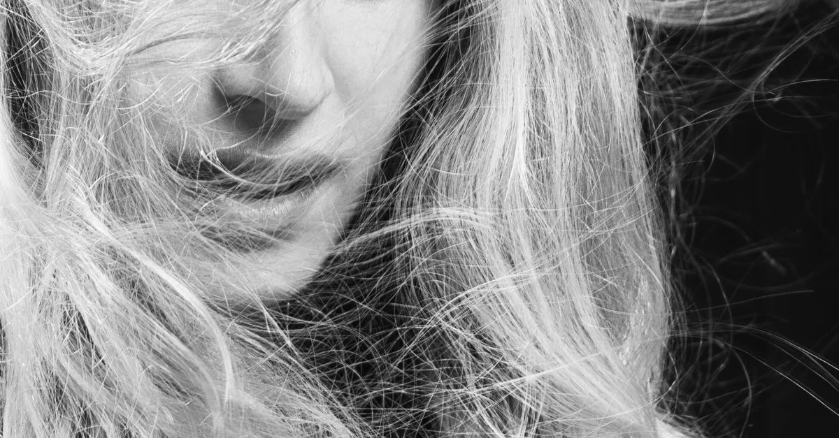 Portrait captivant en noir et blanc d'une femme aux cheveux blonds flottants, exprimant émotion et mouvement.