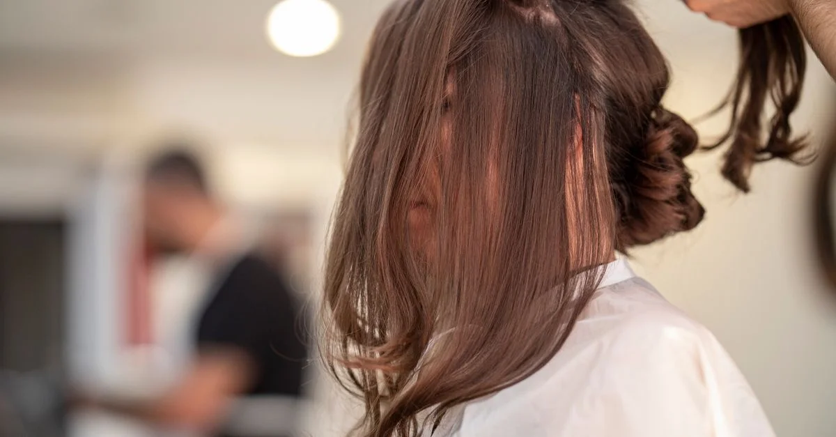 Vue de côté d'une femme se faisant coiffer par un coiffeur dans un salon moderne.
